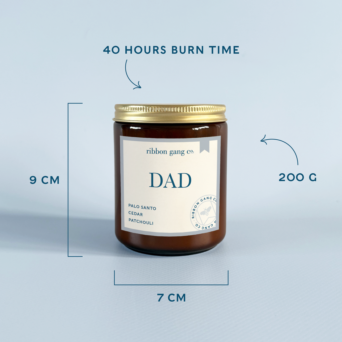An amber glass jar candle with a gold lid and a cream label reading 'DAD' and 'Palo Santo Cedar Patchouli' by ribbon gang co., shown on a light blue background with measurement callouts for 9 cm height, 7 cm width, and 200 g weight, plus text noting 40 hours burn time.