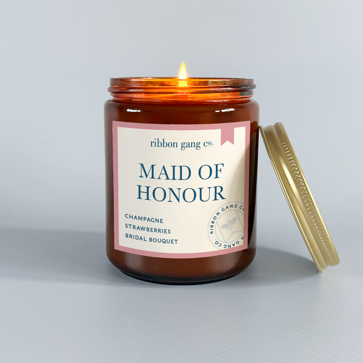 Candle in an amber jar with a 'Maid Of Honour' label by Ribbon Gang Co. on a light gray background.