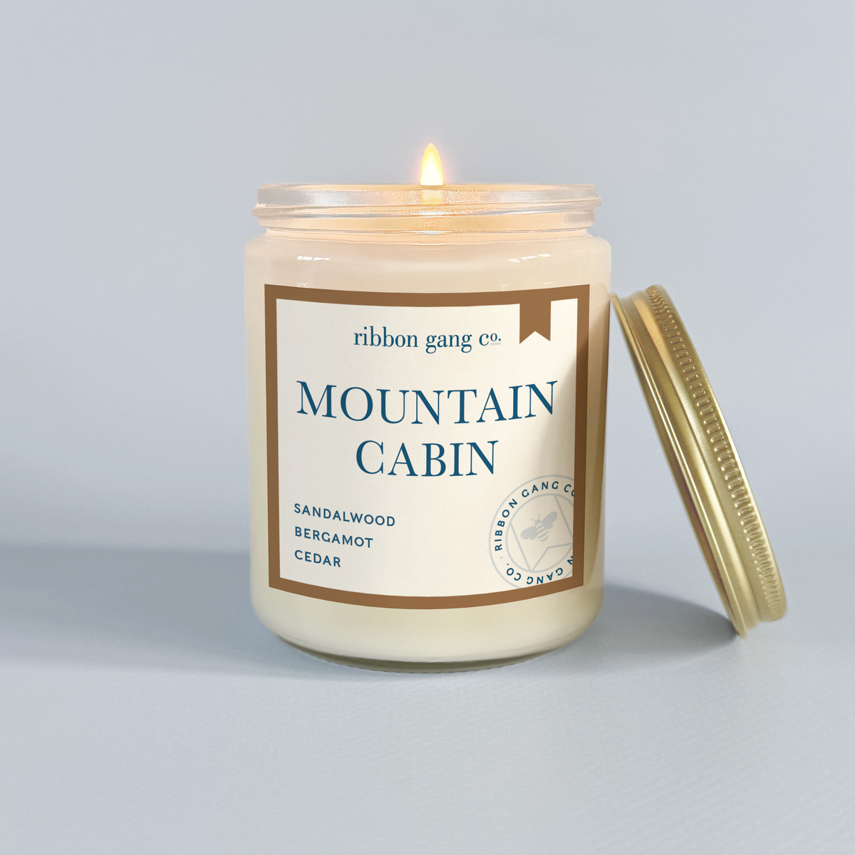 Candle in a jar labeled 'Mountain Cabin' by Ribbon Gang Co. on a light grey background.