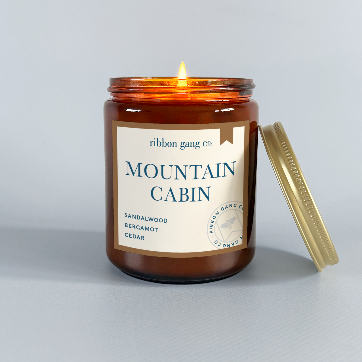 Candle in a brown jar labeled 'Mountain Cabin' by Ribbon Gang Co. on a light grey background.