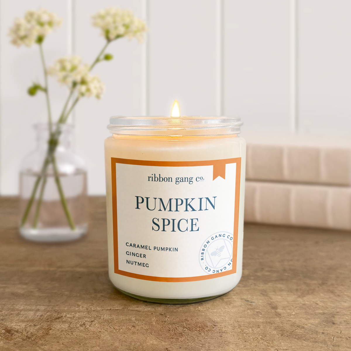Candle labeled 'Pumpkin Spice' by Ribbon Gang Co. on a wooden surface with a blurred background.